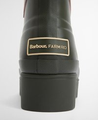 Groene rubberen laars met een textuurafwerking, een bruine leren accent en een gouden label met de tekst "Barbour FARM RIO" aan de zijkant.