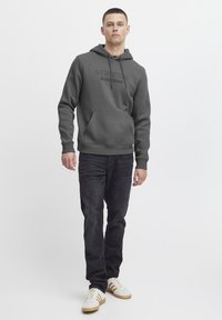 Dark gray hoodie with drawstrings, kangaroo pocket, and printed “NEW YORK BLEND DENIM” logo. Paired with dark jeans and white sneakers.