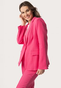 Světle růžový blazer a odpovídající kalhoty vyrobené z lněné směsi. Blazer má klopové límce a kapsy s klopami; dobře padnoucí střih s dlouhými rukávy.