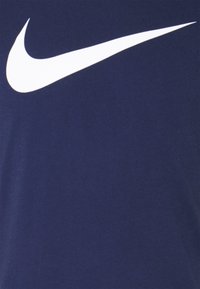 Valkoinen Nike-swoosh-logo keskitetty tummansinisen kankaan taustalle.