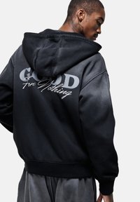 Sweatshirt à capuche noir avec un design dégradé, "GOOD" en lettres grises en gras, et "for Nothing" en police manuscrite au dos.