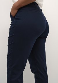 Navy blue pants made of a stretchy fabric, featuring side pockets and a fitted design, with a smooth texture and minimalistic styling.