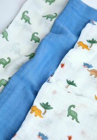 Tři jemné, texturované mušelínové látky: jedna světle modrá, dvě s bílým pozadím, na kterých jsou zelení dinosauři, oranžové kočky a palmy.