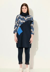 Marinstil blus med geometriskt mönster i blått och kräm, med en blå ficka. Kombineras med marinblå leggings och krämfärgade slip-on skor.