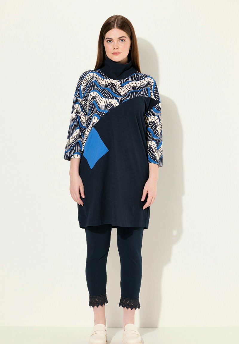Marinstil blus med geometriskt mönster i blått och kräm, med en blå ficka. Kombineras med marinblå leggings och krämfärgade slip-on skor.