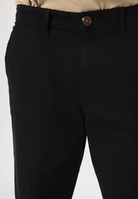 Calças de algodão pretas com fecho de botão, bolsos frontais e uma textura suave. Design simples com detalhes de costura visíveis.