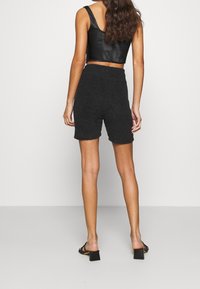 Svart, texturerade shorts i knälängd med hög midja och avslappnad passform. Matchas med en åtsittande svart lädercrop top och klacksandaler med blockklack.