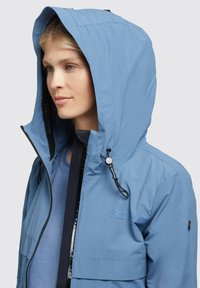Light blue waterproof jacket with adjustable hood, front zipper, and chest pocket. Features a textured fabric and elastic drawstrings.