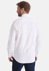 Weißes Langarmshirt mit geradem Schnitt, Knopfmanschetten und Rückenkoller, getragen mit dunklen Jeans. Aus weichem Baumwollstoff.