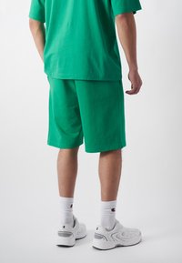 Grünes Baumwoll-T-Shirt und passende Shorts in lockerem Schnitt. Auffällig sind die kurzen Ärmel und der Saum, der leicht unterhalb der Taille endet.