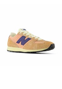 Athletischer Sneaker mit einem Obermaterial in Pfirsich- und Tan-Tönen mit Textur, einem lila "N"-Logo, cremefarbenen Schnürsenkeln und einer schwarzen Gummiaußensohle.