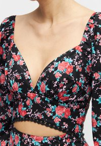 Černý květinový crop top s výraznými růžovými a tyrkysovými růžemi, hlubokým výstřihem do V, puff rukávy a vlnitým krajkovým lemem na spodním okraji.