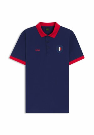 Polo bleu marine avec col et bordures de manches rouges, trois boutons, texte "BOSS" rouge et petit logo en forme d’écusson bleu, blanc et rouge sur la poitrine.