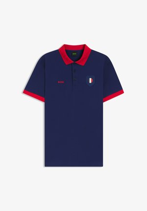Marineblauw poloshirt met rode kraag en mouwranden, drie knopen, rode "BOSS" tekst en een klein schildlogo in blauw, wit en rood op de borst.