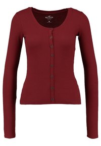 Pitkähihaisen, ribbattun kardiganin väri on burgundi, ja siinä on pyöreä pääntie sekä napitettavat etuosat, joissa on kuusi mustaa nappia. Pehmeä materiaali.