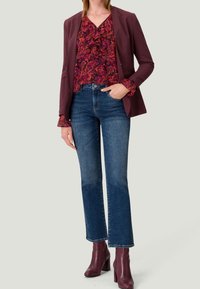 Blazer bordeaux sur un chemisier à volants floral. Jean bleu évasé avec un léger délavage. Bottines à talons bourgogne. Tissu lisse et coupe ajustée.