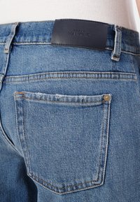 Light blue denim jeans featuring a classic five-pocket design, with visible stitching and a dark leather brand patch on the back waist.