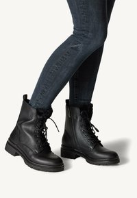 Botas negras hasta el tobillo con un acabado de cuero liso, forro interior suave, cordones en la parte delantera y cremallera lateral. Suela gruesa con relieve para mayor agarre.
