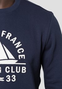 Sweat-shirt bleu marine avec texte blanc "FRANCE YACHTING CLUB 33" et un motif de voilier blanc sur la poitrine.