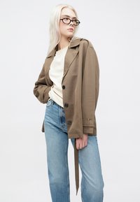Brown, lightweight trench coat with a collared design, single-breasted buttons, and a tie waist, paired with light blue jeans and a cream top.