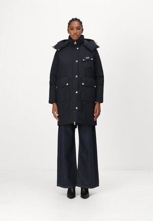 Doudoune noire avec fermeture éclair et pression, capuche, accents dorés et poches avant. Associée à un pantalon en denim noir à jambe large.