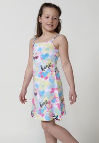 Buntes, ärmelloses Kleid mit einem Herzmuster in Pink, Blau und Gelb sowie schwarzen Textakzenten. Leichtes Baumwollmaterial, knielang.