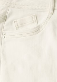 Vitt denimtyg som visar en liten framficka, synlig sömnad och två dekorativa metallstift nära fickan. Slät textur.