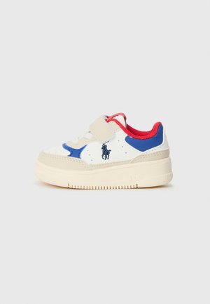 Zapatilla blanca con acentos en azul y rojo, que cuenta con una correa de velcro, puntera redonda, suela texturizada y logo bordado en el lateral.