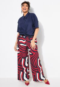 Navy blue short-sleeve button-up shirt tied at the waist, paired with wide-leg pants in red, white, and navy abstract pattern. Red pointed heels.