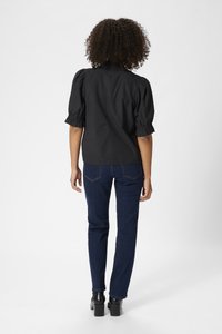 Zwarte blouse met korte, pofmouwen, geplooid rugontwerp, gecombineerd met donkerblauwe rechte jeans en chunky zwarte haklaarzen.
