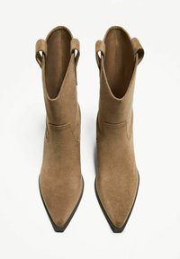 Stivaletti alla caviglia in suede marrone con punta affusolata e doppi tiranti, caratterizzati da una texture liscia e dettagli di cucitura minimi.