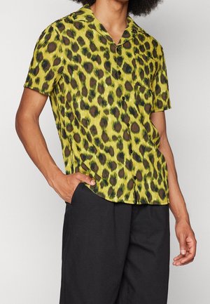 Chemise à manches courtes en tissu léger et transparent, de couleur jaune-vert vif avec un motif de léopard noir et un ourlet droit.