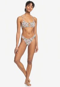 Blomstrete bikini sett med mønstret topp med tynne stropper og en åpning i midten, kombinert med lavt liv bikiniunderdel. Fargene inkluderer rosa, blå og gul.