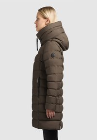 Brun puffy jakke med hætte, med vandret syninger, et sort logo-patch på ærmet og lynlåsede sidelommer.