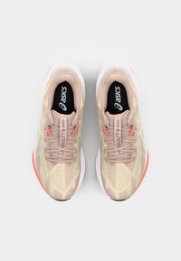Beige sportieve schoenen met een gestructureerde bovenkant, voorzien van diamantpatronen. Roze accenten op de veters en de buitenzool. Zwart logo op de binnenzool.