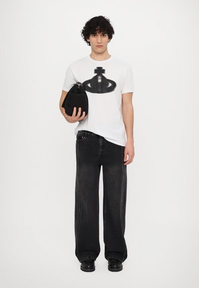 T-shirt alb cu design grafic negru, asortat cu pantaloni negri din denim largi și pantofi negri masivi, ținând o geantă neagră.