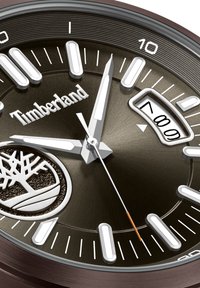 Reloj Timberland con caja metálica redonda de color marrón, esfera marrón oscura, índices horarias plateados, manecillas blancas y una visualización de la fecha a las tres en punto.