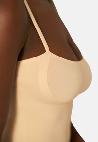 Top senza maniche in nude, con spalline sottili, texture liscia e forma sagomata, progettato per una vestibilità affusolata.