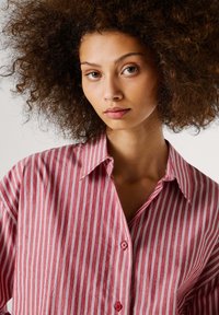 Camisa de botones a rayas rojas y blancas con collar, que presenta una textura suave y botones visibles en la parte delantera.