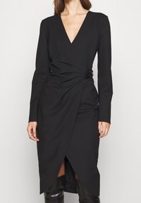 Schwarzes, langärmliges Wickelkleid mit tiefem V-Ausschnitt, das über ein verdrehtes Vorderteil und eine seitliche Schnalle verfügt, aus glattem Stoff gefertigt.