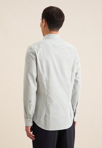 Camicia a righe button-up in verde chiaro e bianco. Presenta una vestibilità sartoriale, maniche lunghe e polsini con bottoni, con un orlo arrotondato.