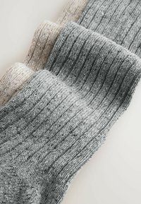 Drei Paar gestrickte Socken in hellbeige und grauen Farbtönen, mit geripptem Muster und einem weichen, melierten Garnlook.