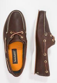 Scarpe da barca in pelle marrone con suole in gomma bianca, lacci marroni e occhielli in tonalità oro. Presentano una soletta testurizzata arancione.