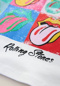 T-shirt med farverige Rolling Stones logo designs mod en hvid baggrund med en tekstureret grafik og fed sort tekst.