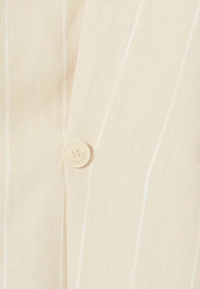 Tela de beige claro con una sutil textura acanalada, que presenta un botón redondo de color claro en el centro. Finas rayas blancas corren verticalmente.