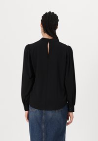 Fekete, hosszú ujjú blúz puffos ujjakkal, magas gallérral és hátul gombos záródással, denim szoknyával párosítva. Texturált anyag.