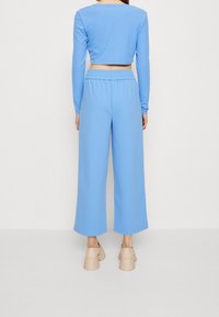 Jasnoniebieski krótki top z długim rękawem o teksturze prążkowanej, zestawiony z pasującymi spodniami typu wide-leg. Płaskie buty w neutralnym kolorze.