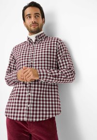 Camicia a quadri rossa e bianca con maniche lunghe e colletto, abbinata a pantaloni in velluto a coste bordeaux. Presenta un orlo arrotondato.