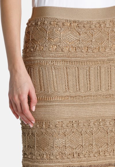 Gehaakte tan rok met complexe textuurpatronen, een brede elastische tailleband en een getailleerde pasvorm die de taille accentueert.