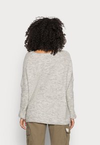 Maglione grigio chiaro dalla vestibilità ampia, con maniche lunghe, scollo ampio e texture morbida, abbinato a pantaloni cargo color oliva.